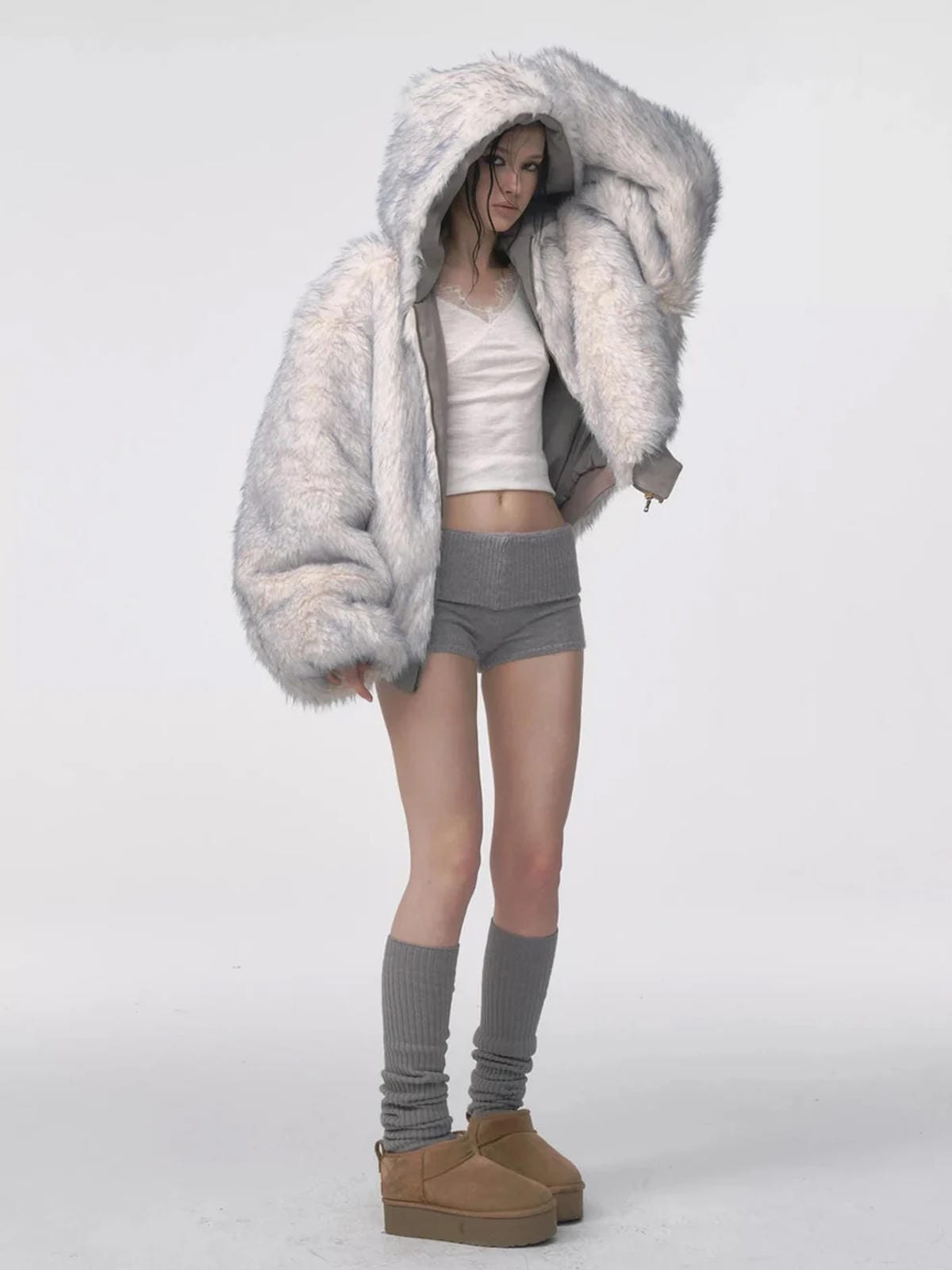 Reversible oversized hooded winter coat for women, gray padded bomber jacket side with white faux fur lining visible, styled with shorts and knee socks
